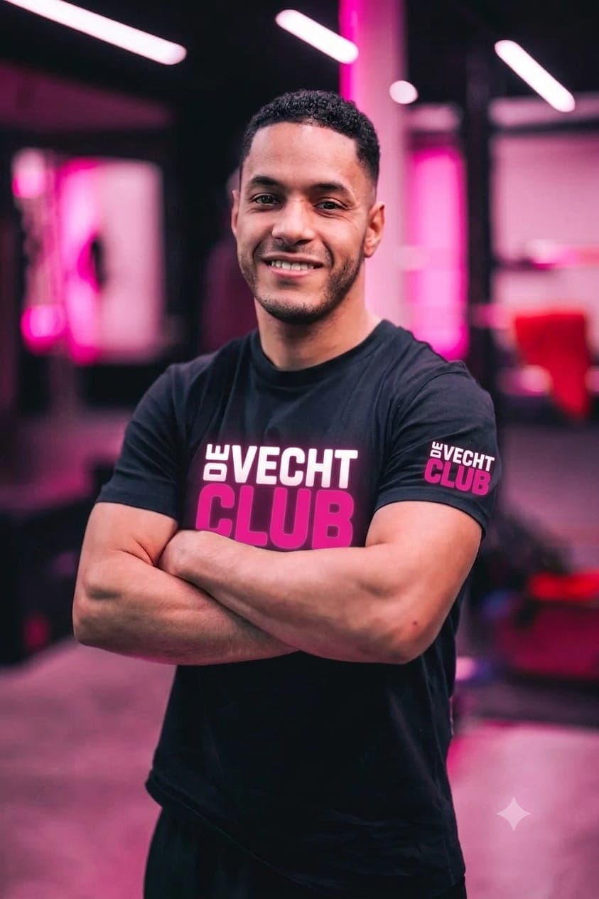 Cedric lachend in de zaal, in een zwart De Vechtclub-shirt met de armen over elkaar